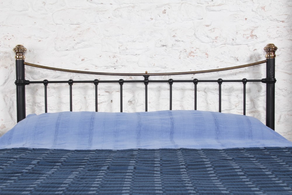 An Edwardian black iron and brass king-size bedstead featuring a curved dip rail and brass corner finials. View V
