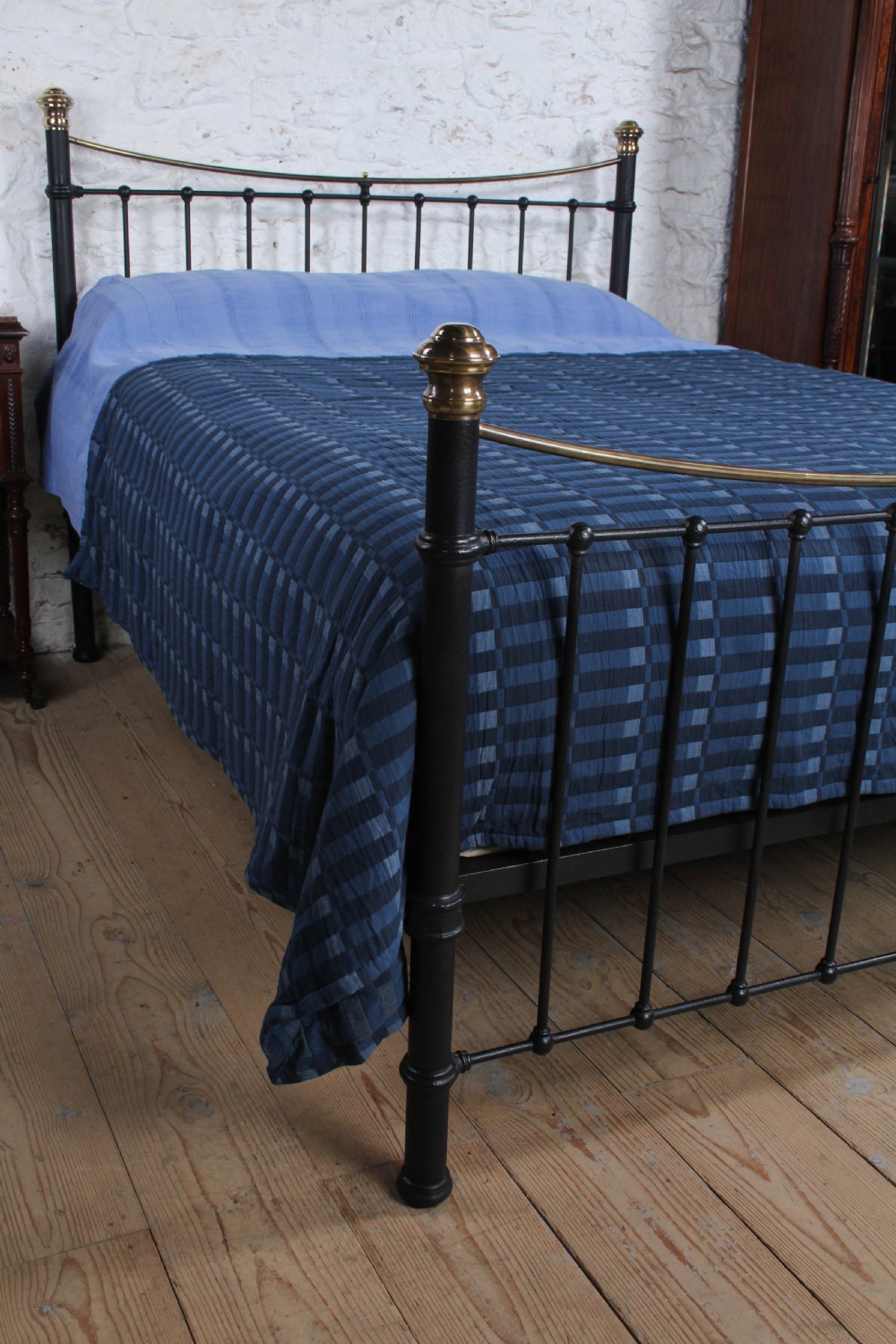 An Edwardian black iron and brass king-size bedstead featuring a curved dip rail and brass corner finials. View VI
