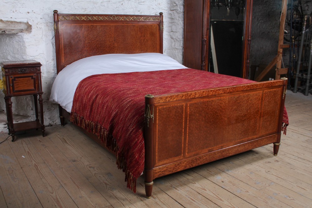 An antique French mahogany king-size bed frame featuring inlaid wood borders, decorative brass mounts, and fluted corner posts.