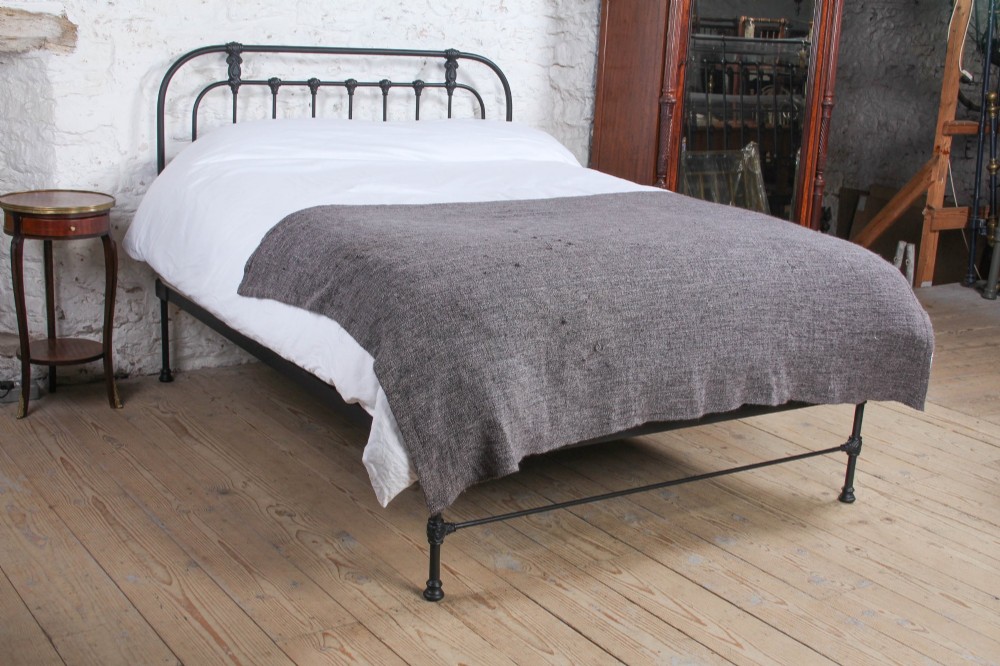 A Victorian Art Nouveau style black cast iron king size bed frame featuring vertical spindles and decorative joinery details.
