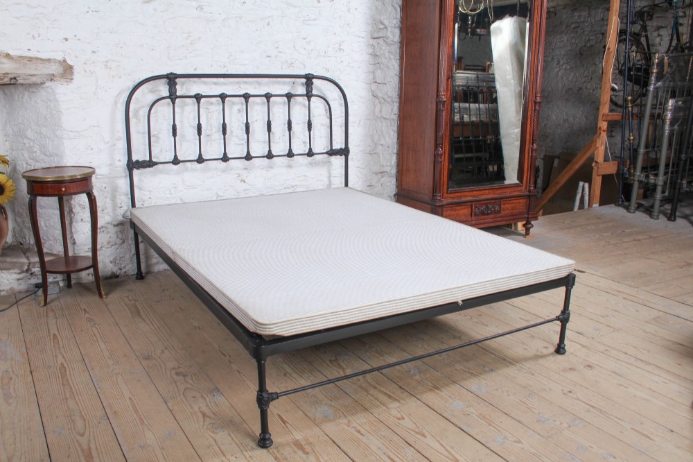 A Victorian Art Nouveau style black cast iron king size bed frame featuring vertical spindles and decorative joinery details. View VIII