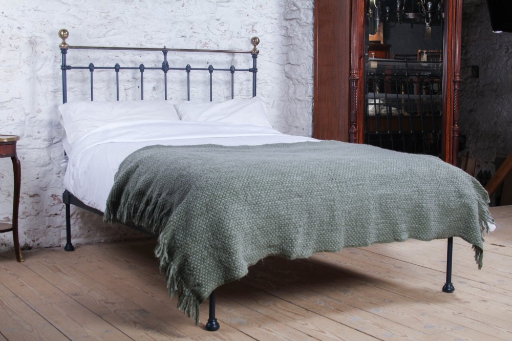 A Victorian double bed frame featuring a dark cast iron headboard with vertical spindles and a polished brass top rail with corner finials.
