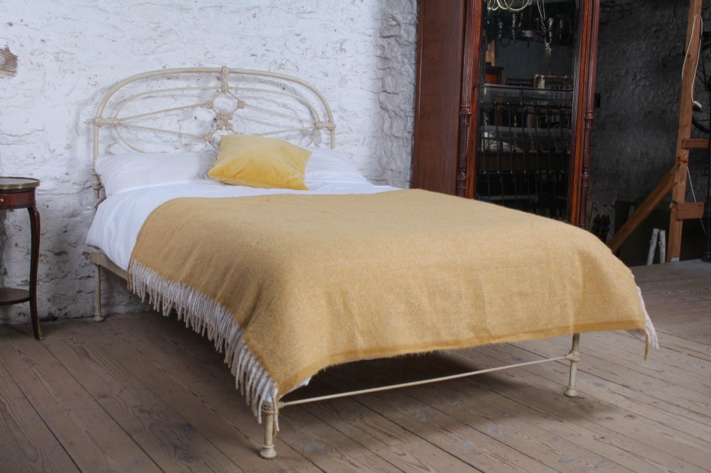 A cream-painted Victorian metal double bed frame featuring a arched wrought iron headboard with decorative cast iron joints.