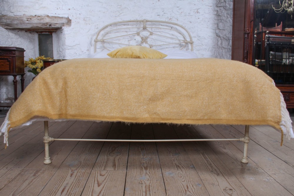 A cream-painted Victorian metal double bed frame featuring a arched wrought iron headboard with decorative cast iron joints. View VI