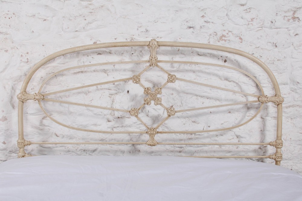 A cream-painted Victorian metal double bed frame featuring a arched wrought iron headboard with decorative cast iron joints. View VII