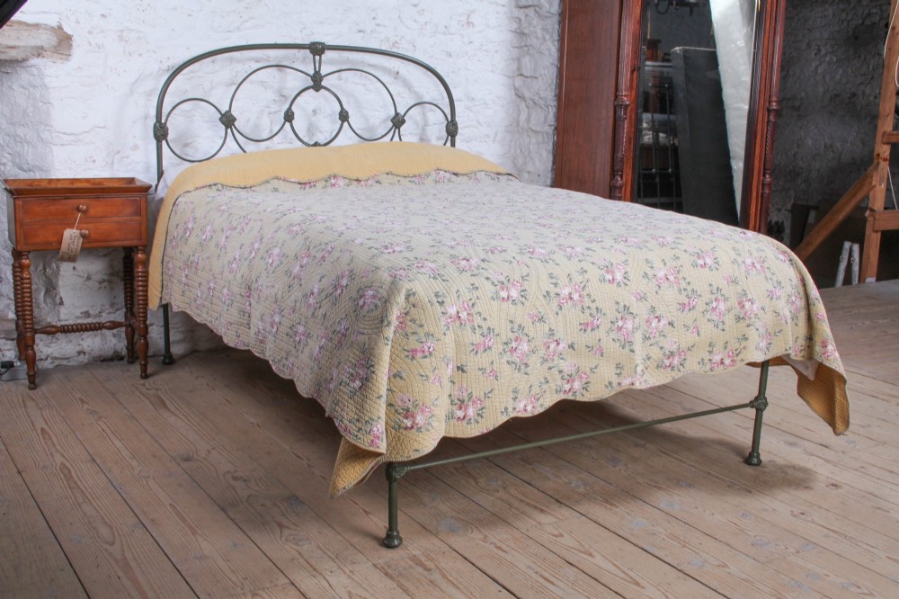 Victorian dark green cast iron double bedstead featuring an arched headboard with decorative scrollwork and a low foot end.