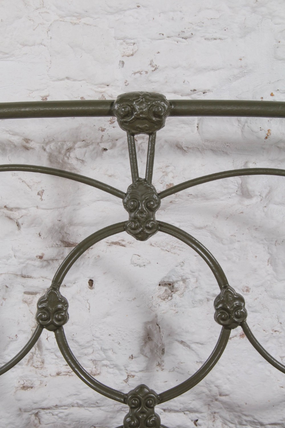 Victorian dark green cast iron double bedstead featuring an arched headboard with decorative scrollwork and a low foot end. View V
