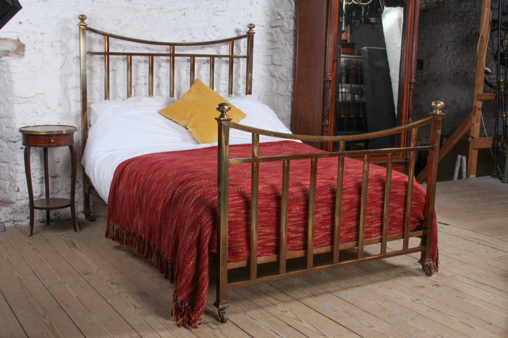 An antique French double bed constructed from brass tubing featuring a curved top rail, vertical spindles, ball finials, and original castors.