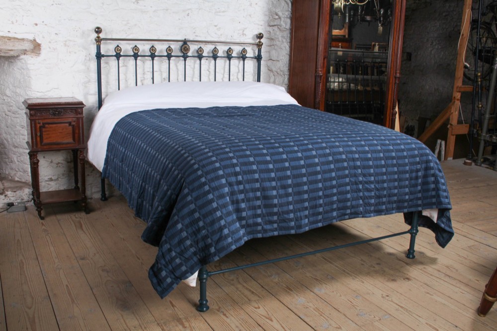 A Victorian king size cast iron bedstead with brass top rail and decorative rosettes, dressed in white and dark blue bedding.