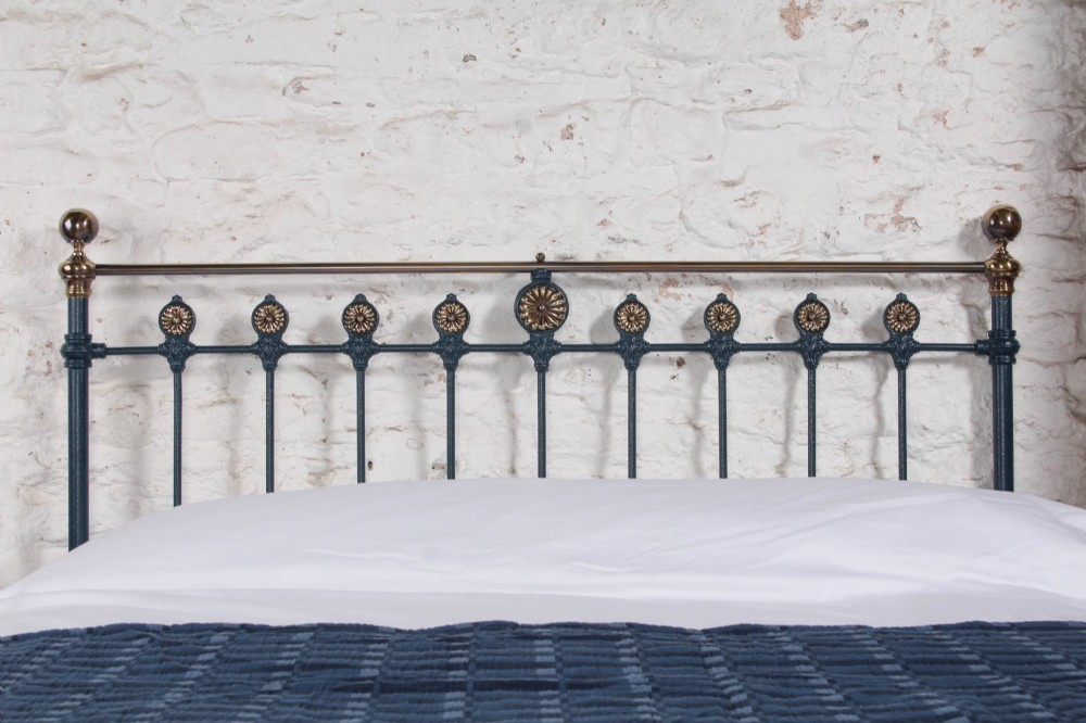 A Victorian king size cast iron bedstead with brass top rail and decorative rosettes, dressed in white and dark blue bedding. View II