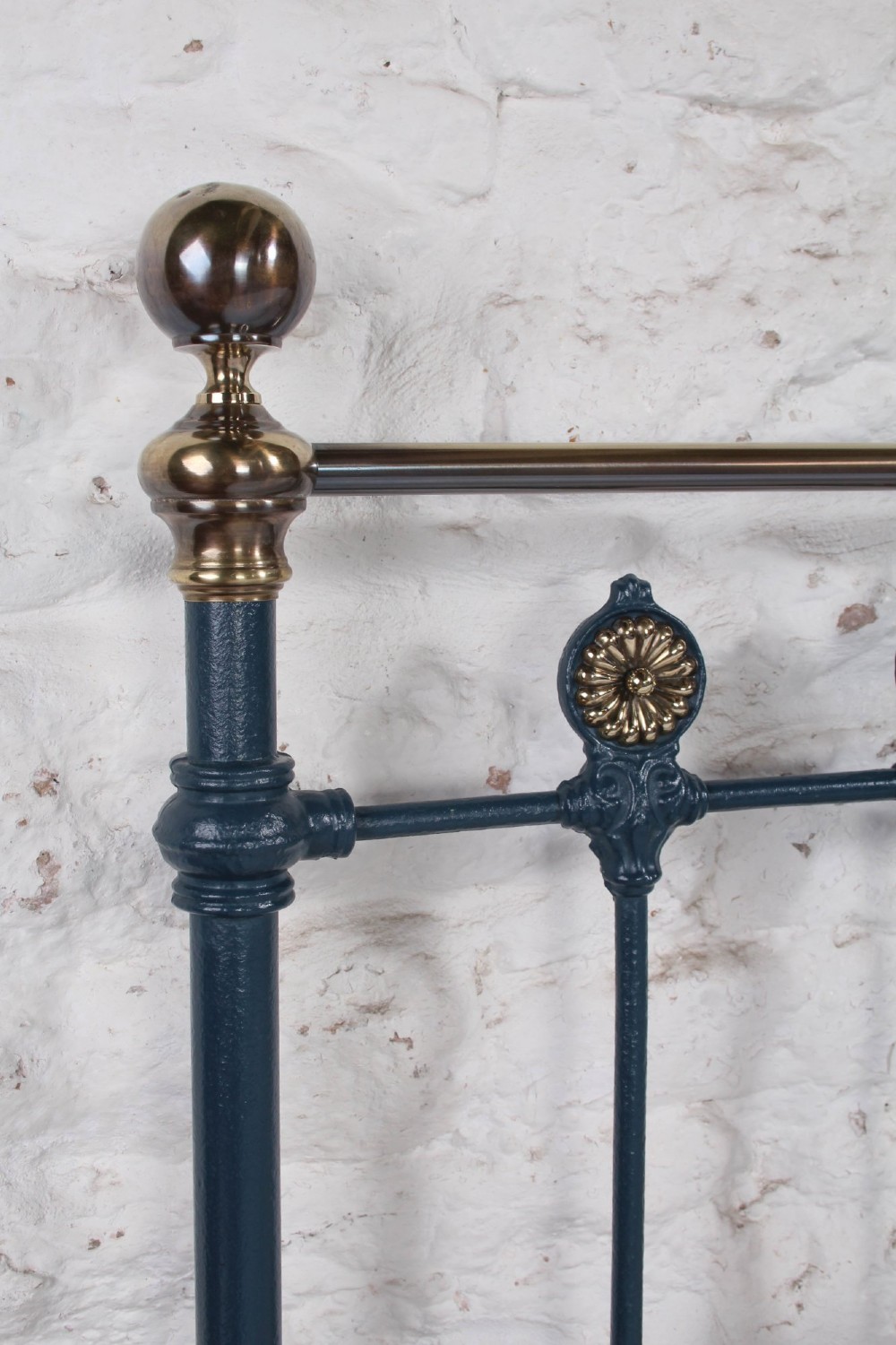 A Victorian king size cast iron bedstead with brass top rail and decorative rosettes, dressed in white and dark blue bedding. View IV