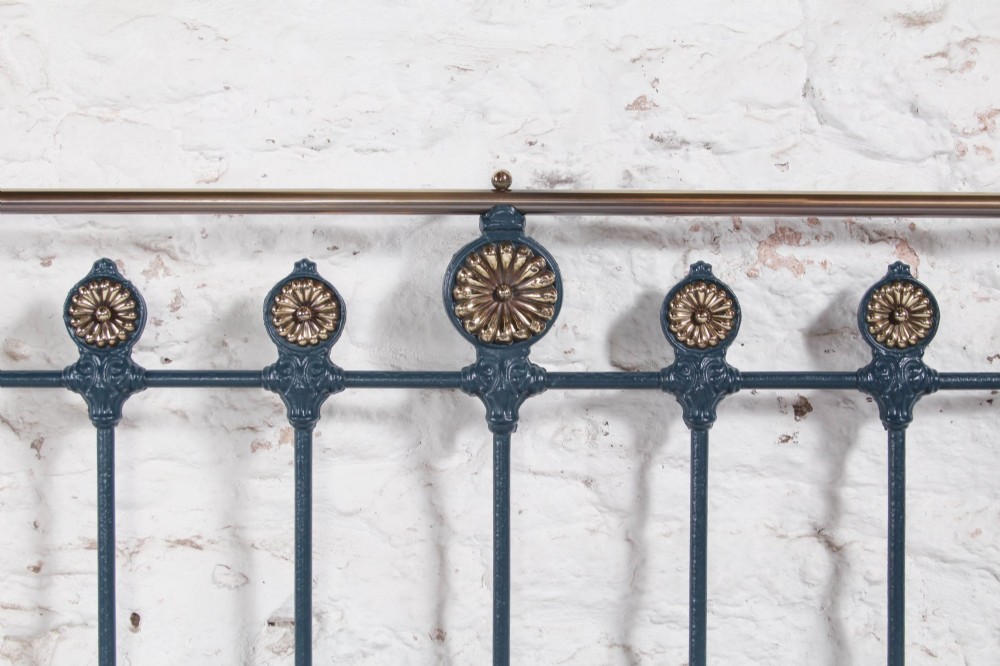 A Victorian king size cast iron bedstead with brass top rail and decorative rosettes, dressed in white and dark blue bedding. View V