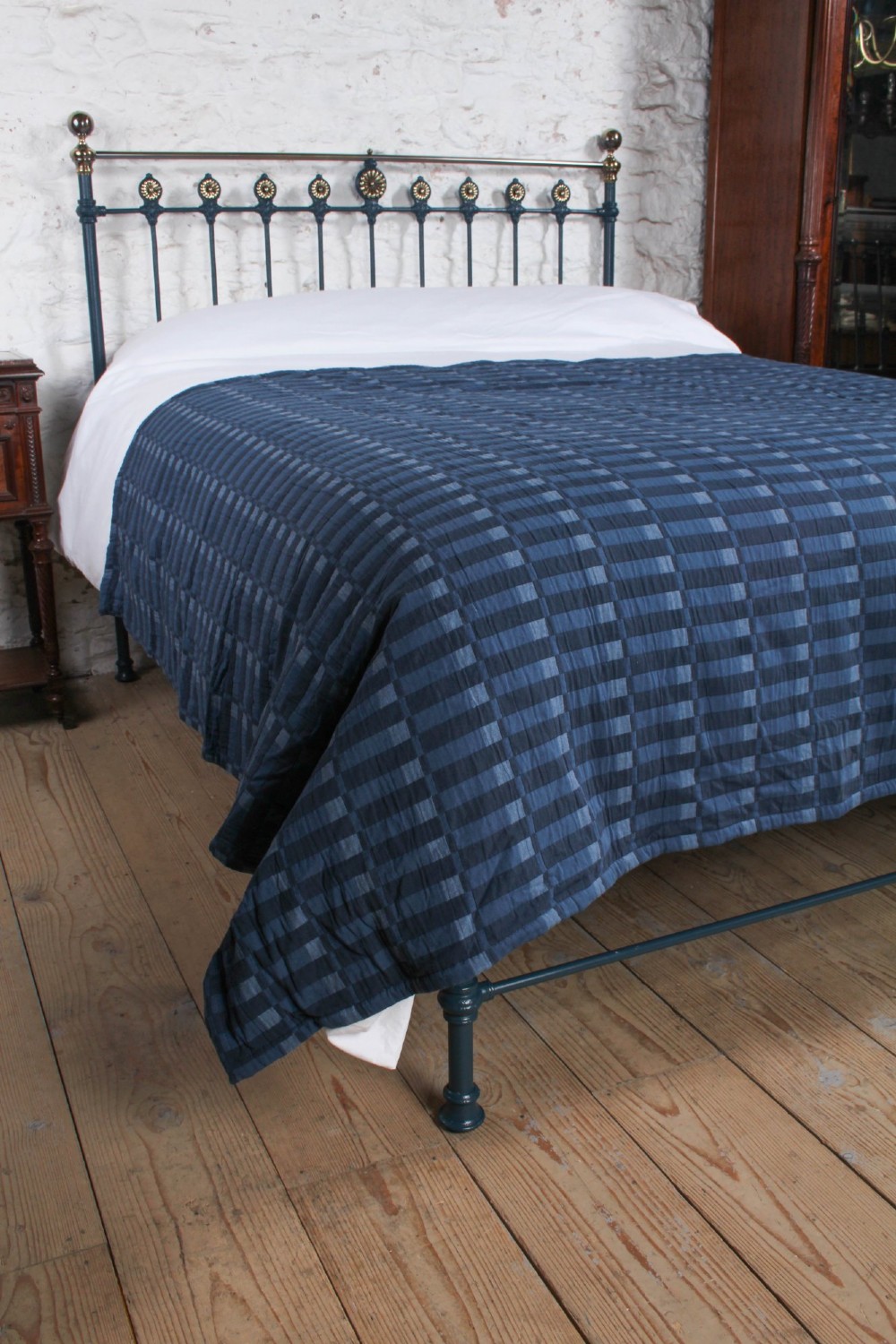 A Victorian king size cast iron bedstead with brass top rail and decorative rosettes, dressed in white and dark blue bedding. View VI