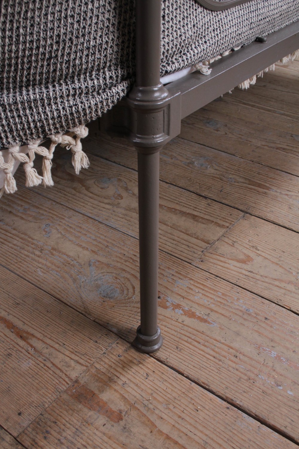 An antique dark grey iron bed frame featuring decorative curved tubing and cast detailing dressed with a textured grey blanket. View IV