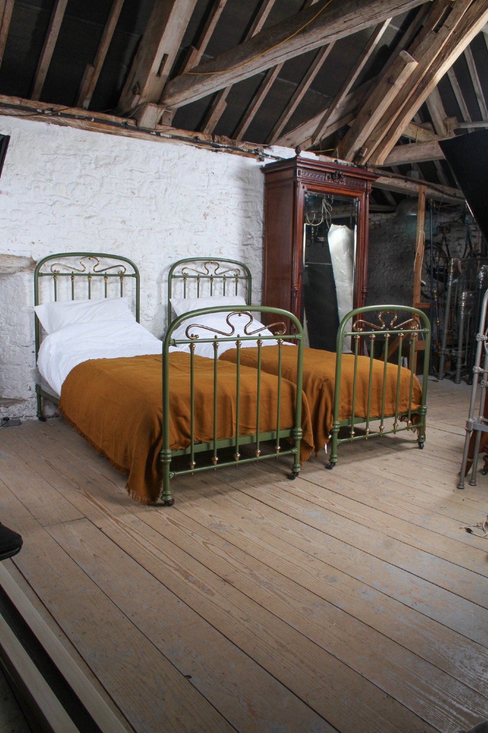 A pair of olive green painted iron single bed frames featuring brass finials, vertical spindles, and decorative scrolled crests. View II