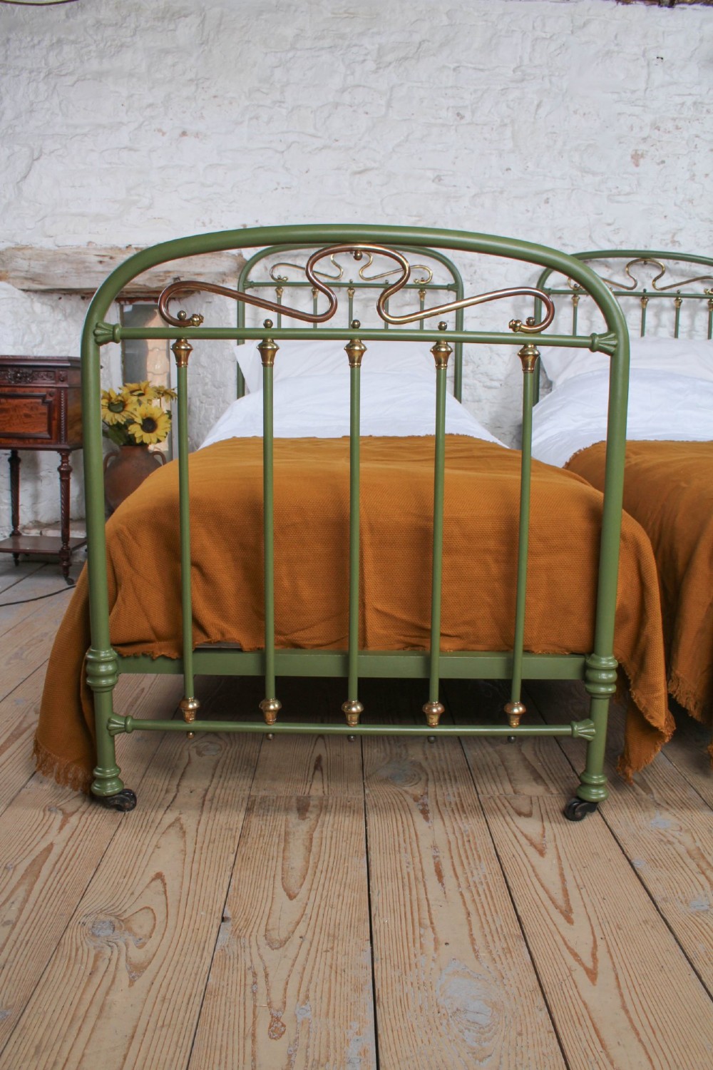 A pair of olive green painted iron single bed frames featuring brass finials, vertical spindles, and decorative scrolled crests. View III