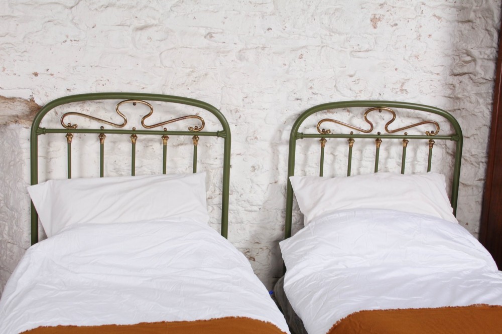 A pair of olive green painted iron single bed frames featuring brass finials, vertical spindles, and decorative scrolled crests. View IV