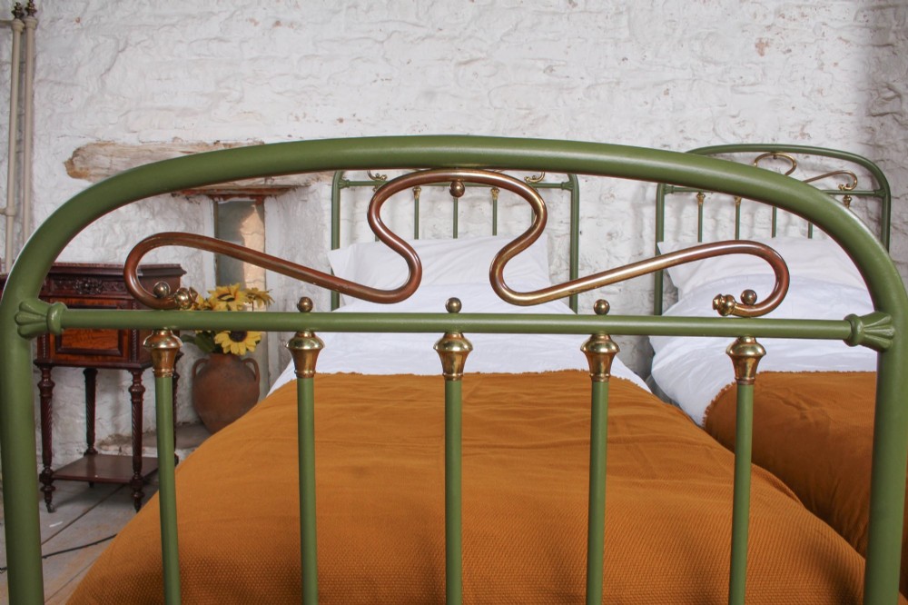 A pair of olive green painted iron single bed frames featuring brass finials, vertical spindles, and decorative scrolled crests. View VI