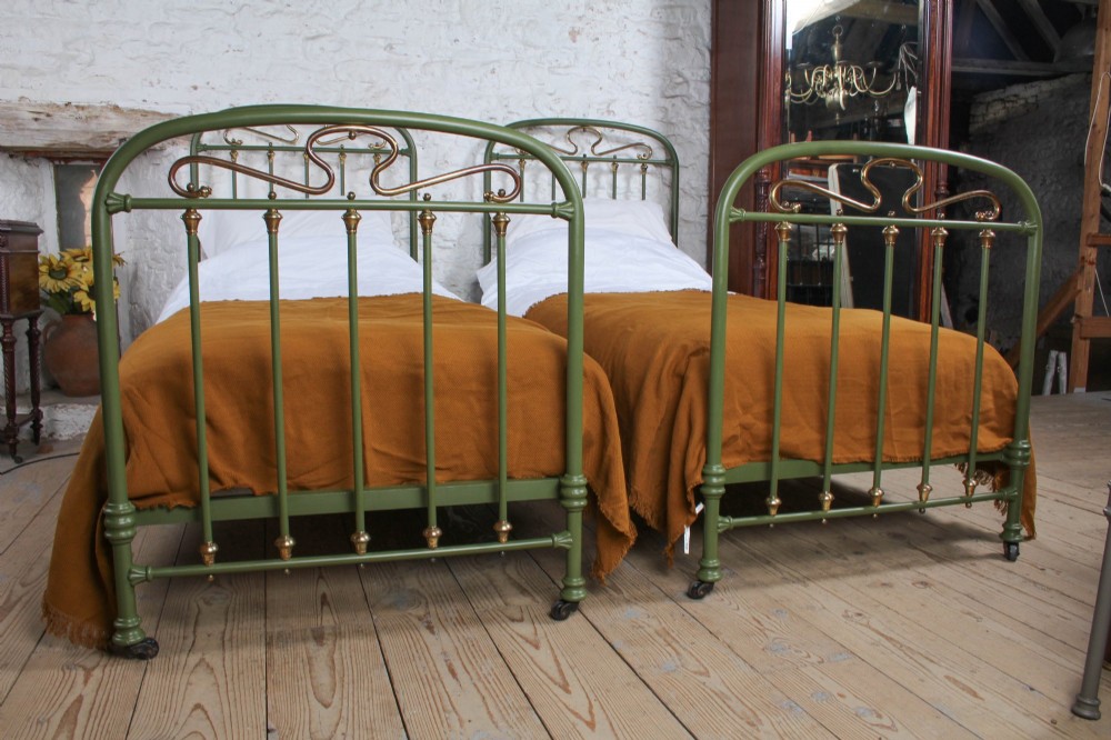 A pair of olive green painted iron single bed frames featuring brass finials, vertical spindles, and decorative scrolled crests. View VIII