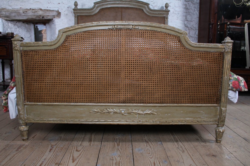 A French Louis XVI style double bed frame with a carved wood surround, woven cane headboard and footboard, fluted legs, and a distressed grey painted finish. View II