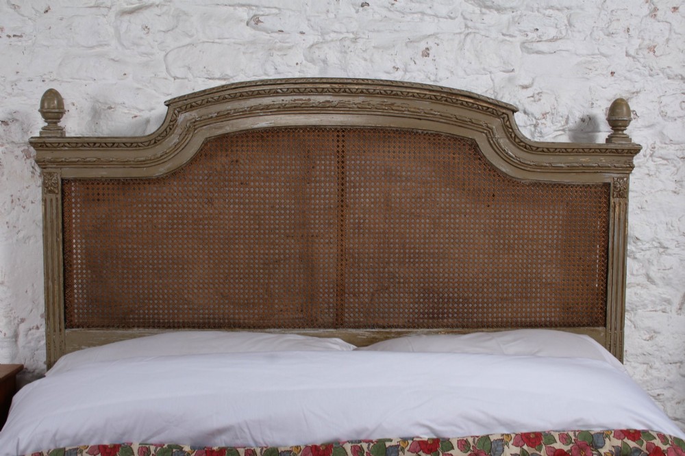 A French Louis XVI style double bed frame with a carved wood surround, woven cane headboard and footboard, fluted legs, and a distressed grey painted finish. View IV