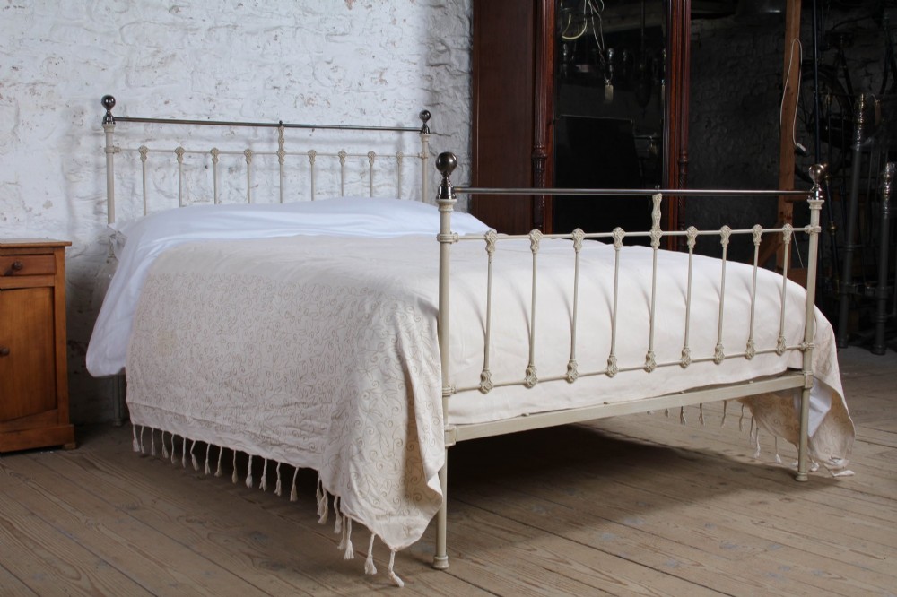 A cream-painted Victorian iron king-size bedstead featuring vertical spindles with cast details and a brass top rail.