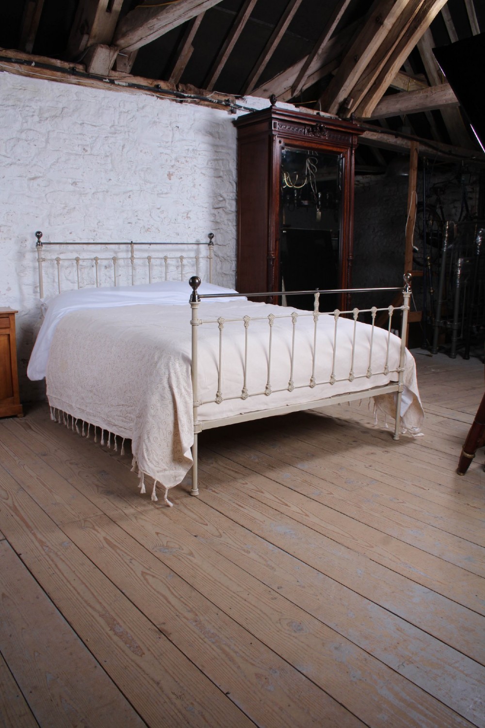 A cream-painted Victorian iron king-size bedstead featuring vertical spindles with cast details and a brass top rail. View II