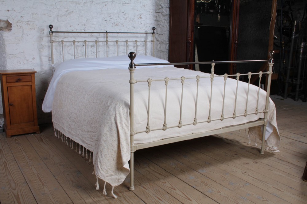 A cream-painted Victorian iron king-size bedstead featuring vertical spindles with cast details and a brass top rail. View III
