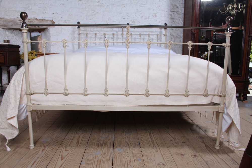 A cream-painted Victorian iron king-size bedstead featuring vertical spindles with cast details and a brass top rail. View IV