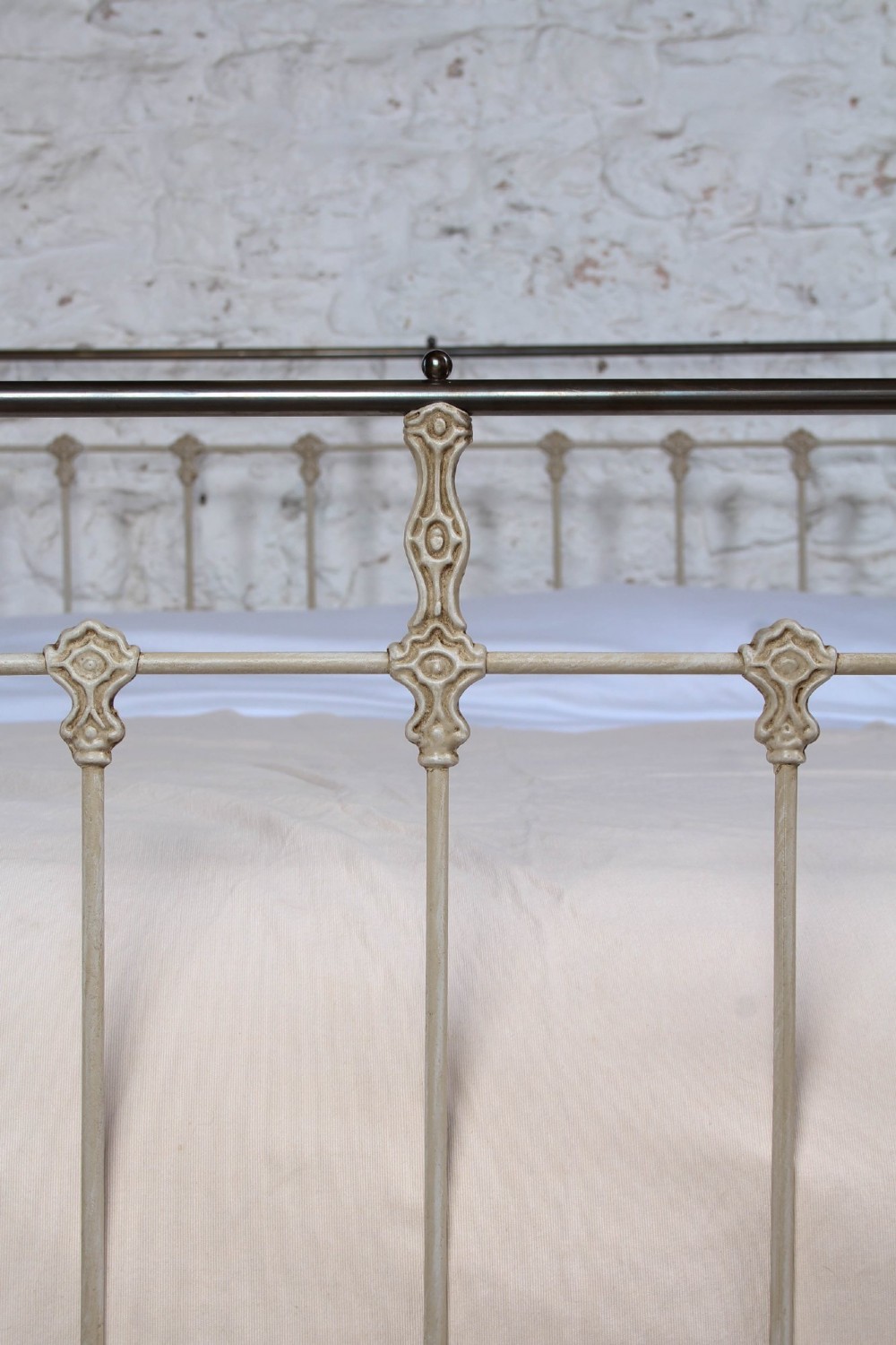 A cream-painted Victorian iron king-size bedstead featuring vertical spindles with cast details and a brass top rail. View V