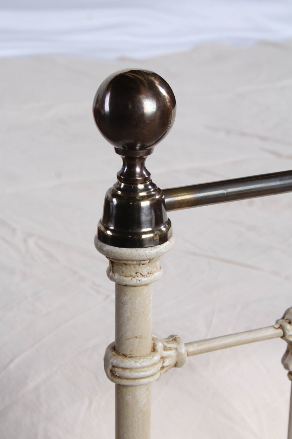A cream-painted Victorian iron king-size bedstead featuring vertical spindles with cast details and a brass top rail. View VI