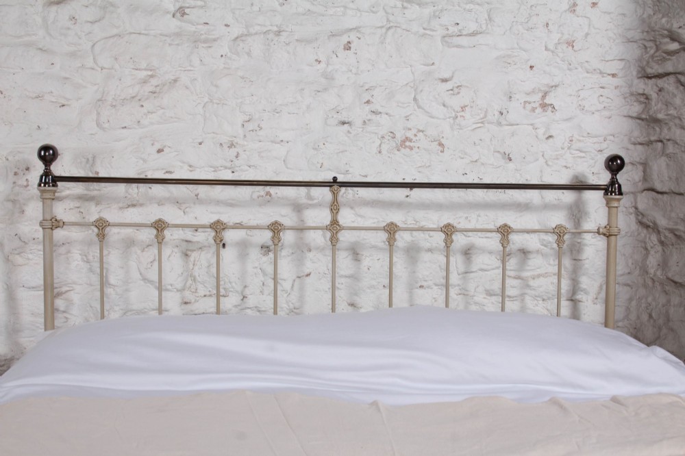 A cream-painted Victorian iron king-size bedstead featuring vertical spindles with cast details and a brass top rail. View VII