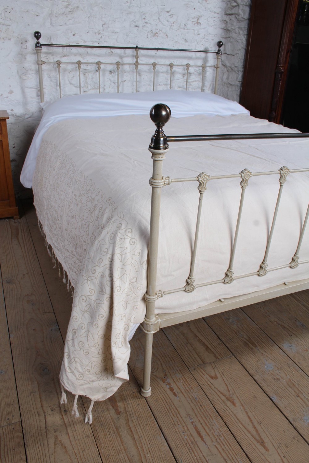 A cream-painted Victorian iron king-size bedstead featuring vertical spindles with cast details and a brass top rail. View IX