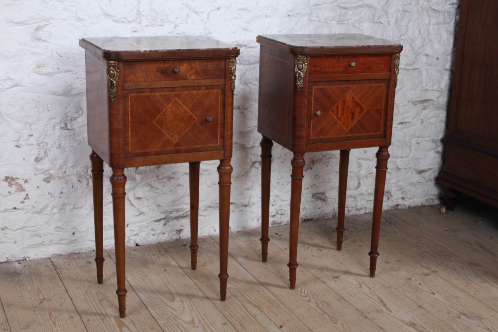 A pair of tall French fruitwood bedside tables featuring square marble tops, diamond parquetry cupboard doors, single drawers, and slender turned tapered legs.