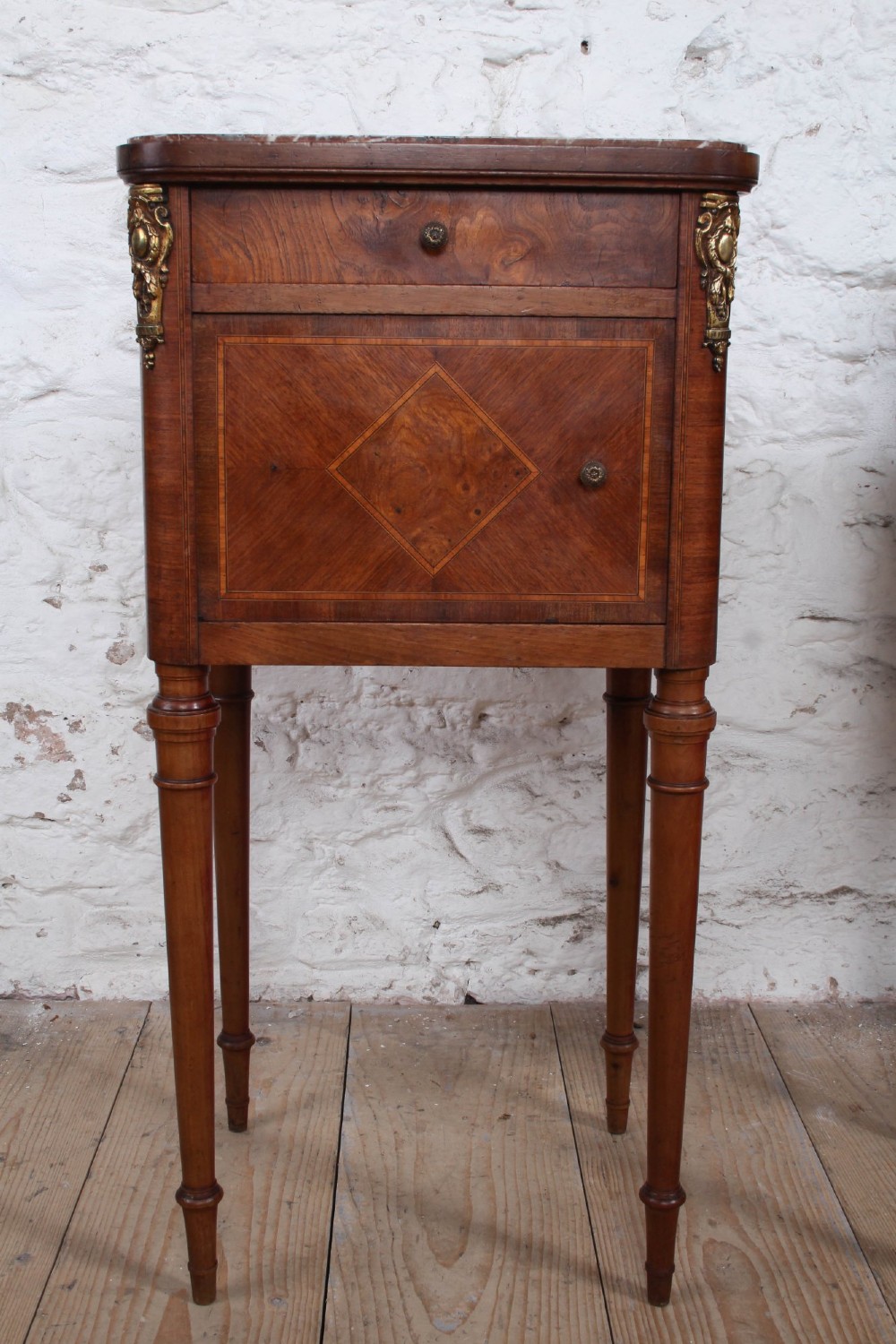 A pair of tall French fruitwood bedside tables featuring square marble tops, diamond parquetry cupboard doors, single drawers, and slender turned tapered legs. View IV