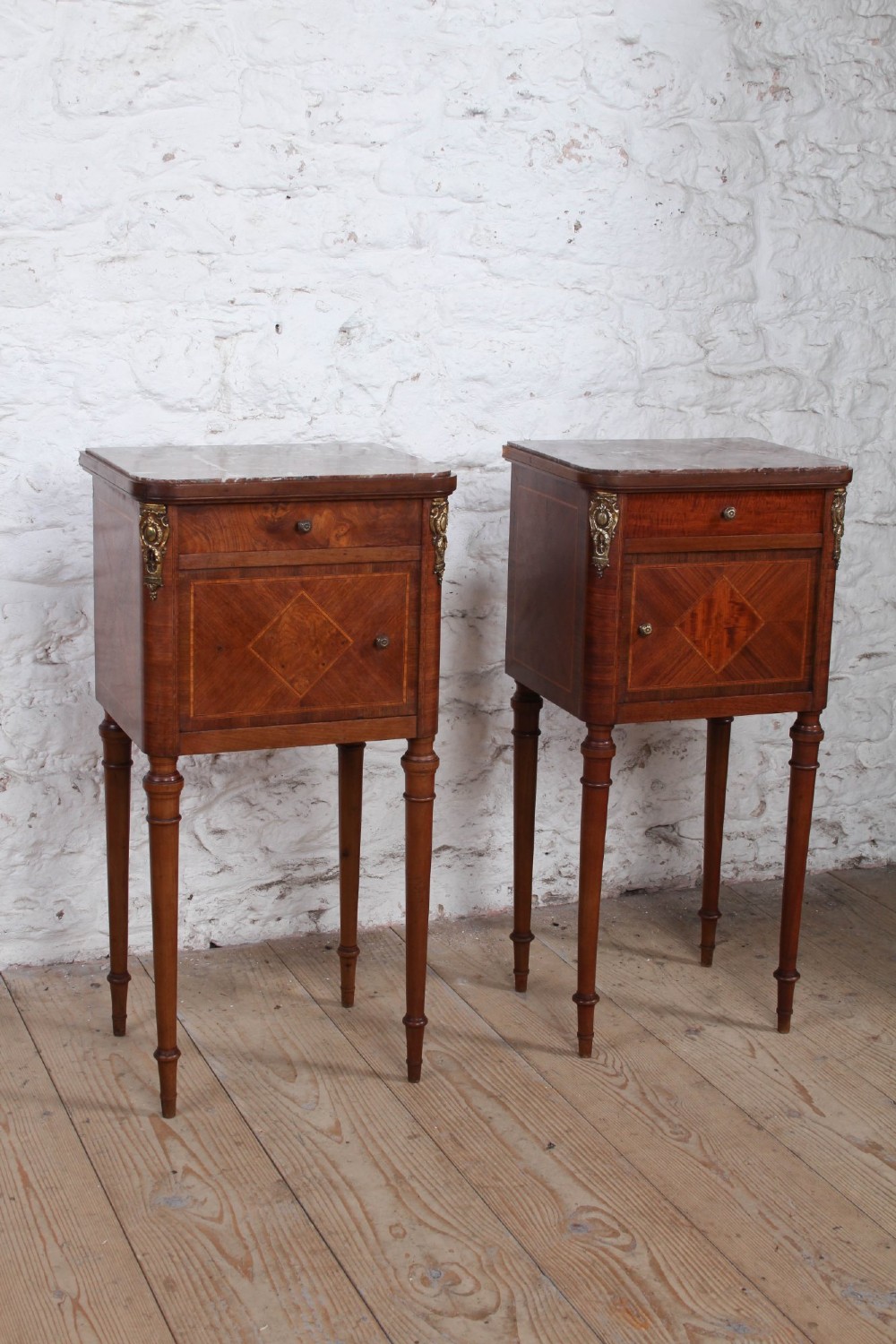 A pair of tall French fruitwood bedside tables featuring square marble tops, diamond parquetry cupboard doors, single drawers, and slender turned tapered legs. View IX