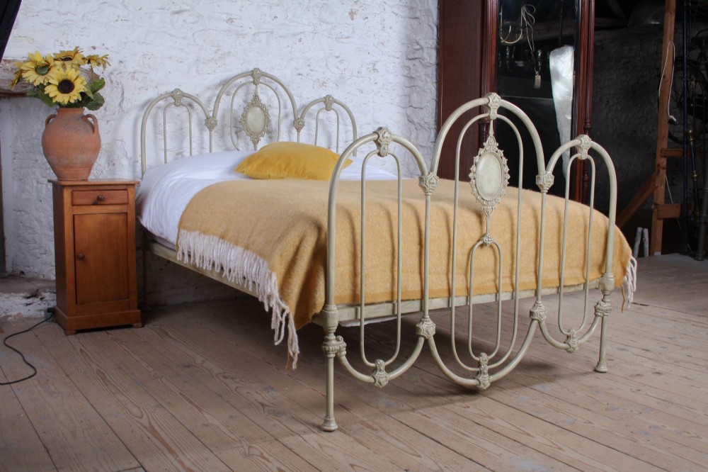 A Victorian cream-painted iron double bed frame featuring a three-hoop headboard and footboard design with central ornate medallions.