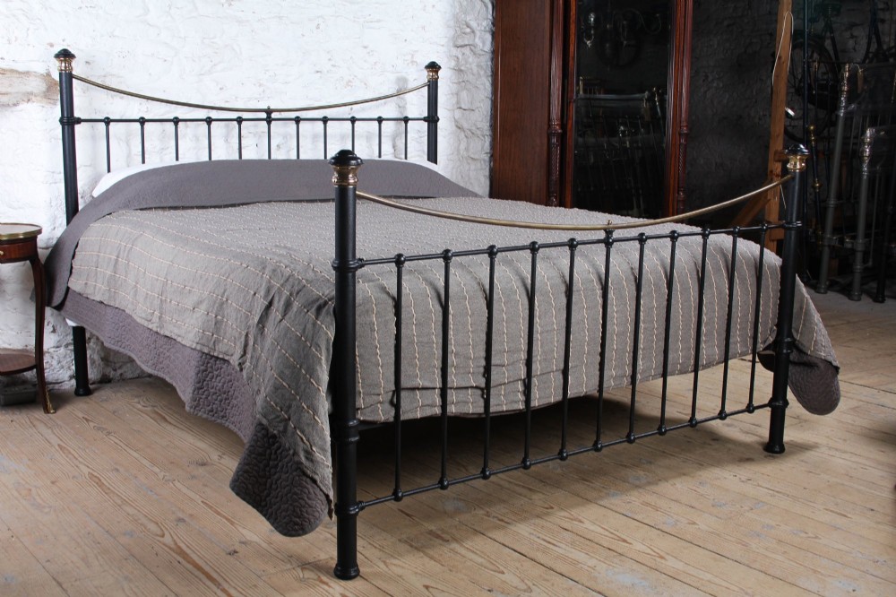 An Edwardian style super king size bed frame made of black painted iron with vertical spindles, topped with curved brass dipping rails and brass finials.