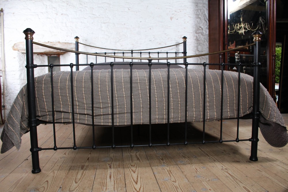 An Edwardian style super king size bed frame made of black painted iron with vertical spindles, topped with curved brass dipping rails and brass finials. View II
