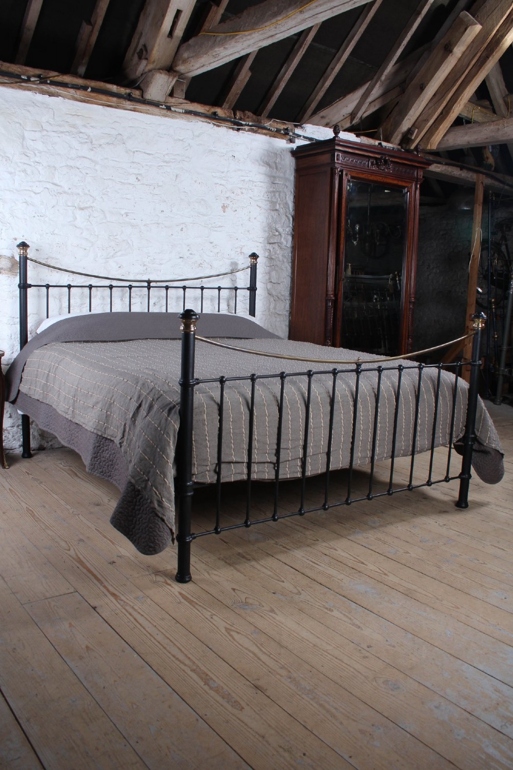 An Edwardian style super king size bed frame made of black painted iron with vertical spindles, topped with curved brass dipping rails and brass finials. View VII