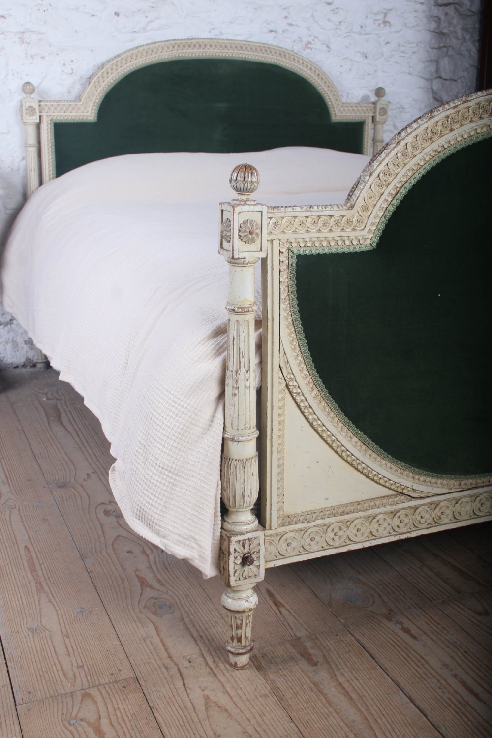 An antique French Louis XVI style bedstead featuring a cream-painted carved wooden frame, fluted posts, finials, and arched headboard and footboard panels upholstered in green velvet. View III