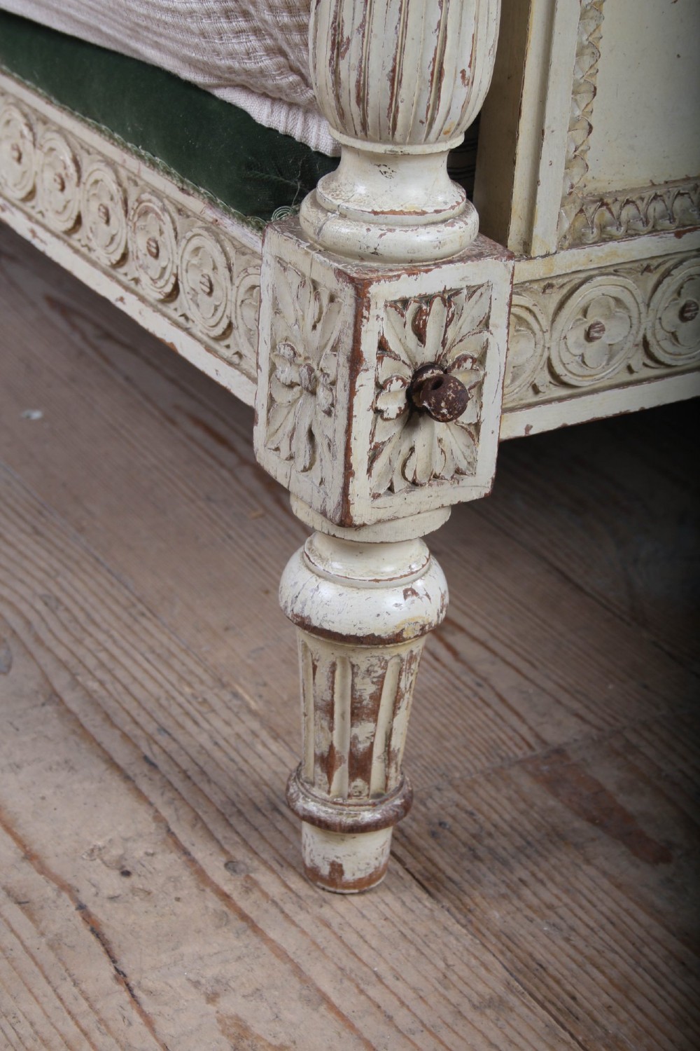 An antique French Louis XVI style bedstead featuring a cream-painted carved wooden frame, fluted posts, finials, and arched headboard and footboard panels upholstered in green velvet. View IV