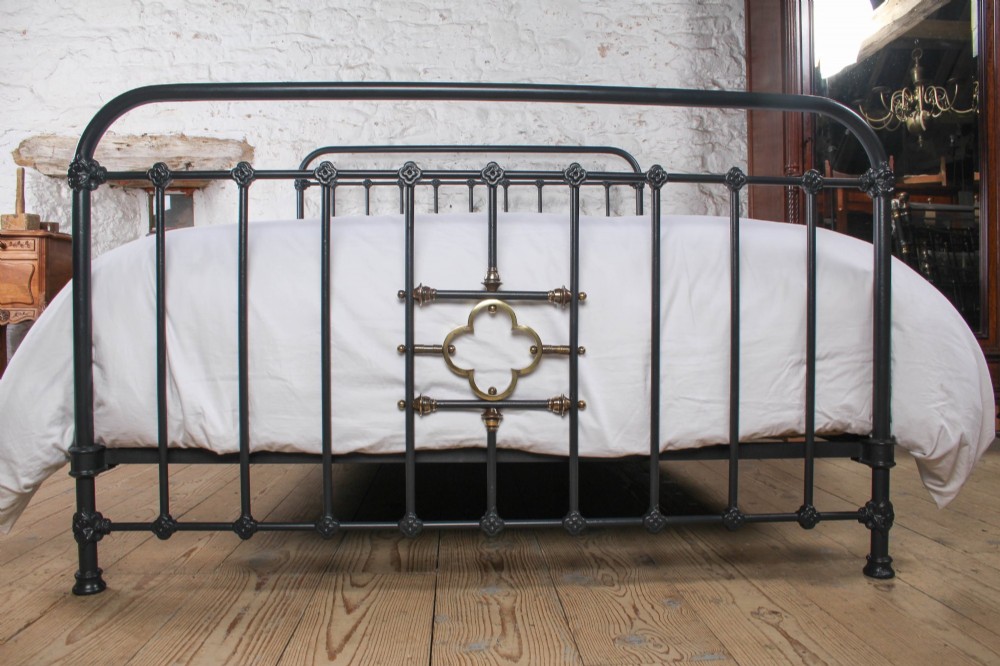 A black iron and brass king-size bed frame featuring vertical spindles and a central brass quatrefoil motif on the footboard. View II