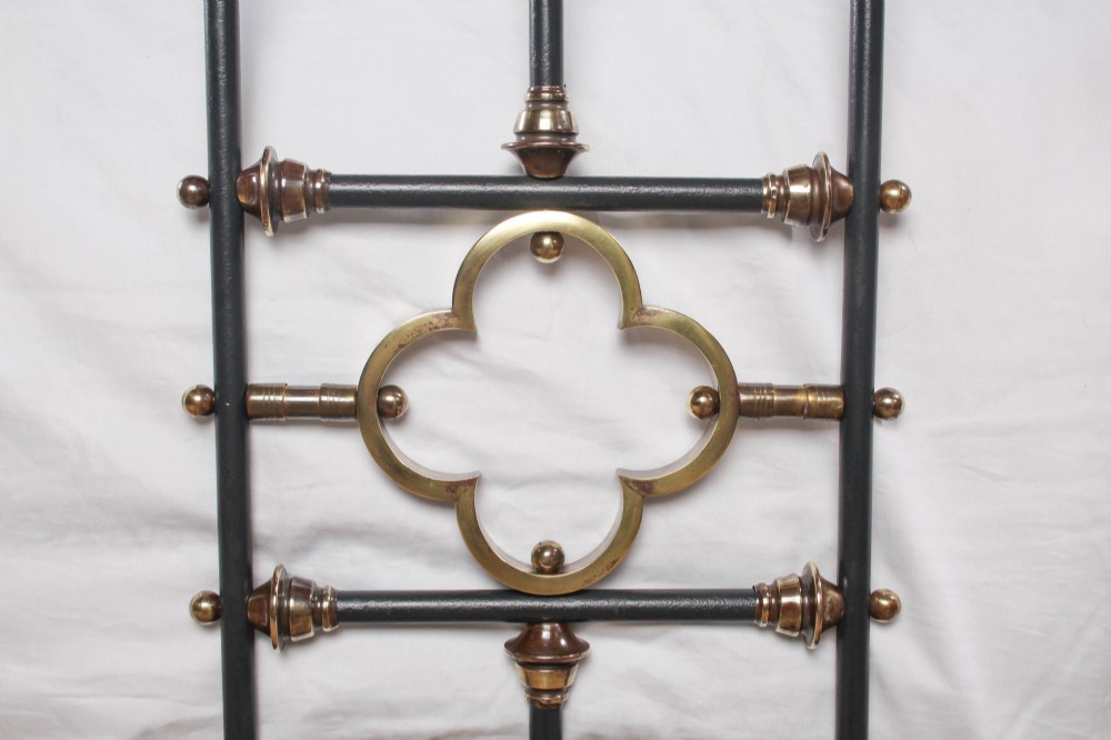 A black iron and brass king-size bed frame featuring vertical spindles and a central brass quatrefoil motif on the footboard. View III