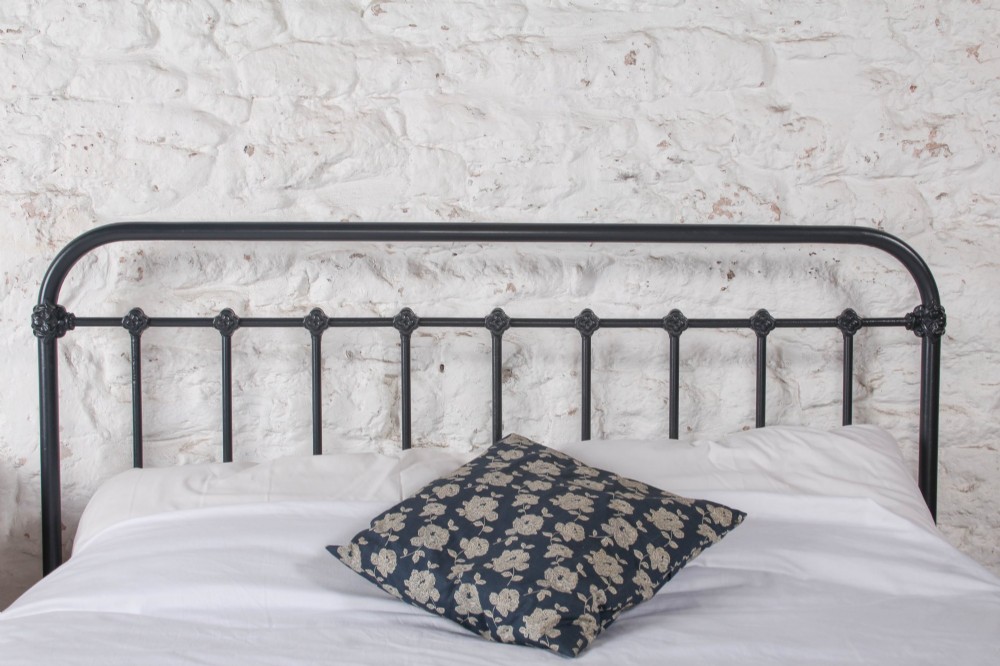 A black iron and brass king-size bed frame featuring vertical spindles and a central brass quatrefoil motif on the footboard. View V