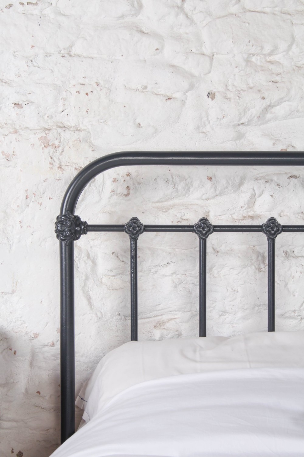 A black iron and brass king-size bed frame featuring vertical spindles and a central brass quatrefoil motif on the footboard. View VII