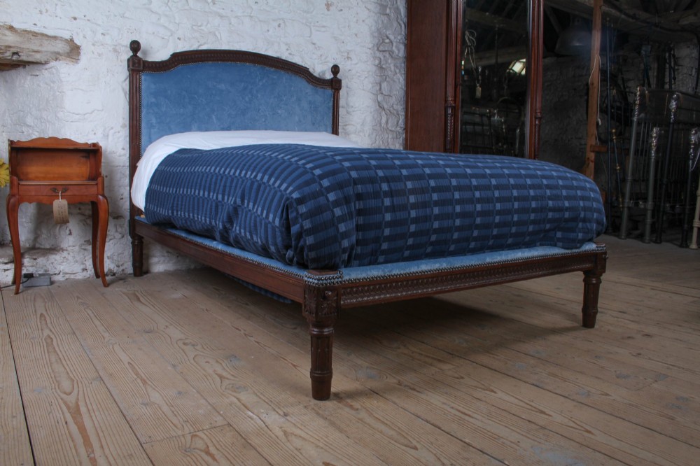 A Louis XVI style oak double bed frame featuring an arched headboard and low footboard upholstered in light blue fabric with trim details.