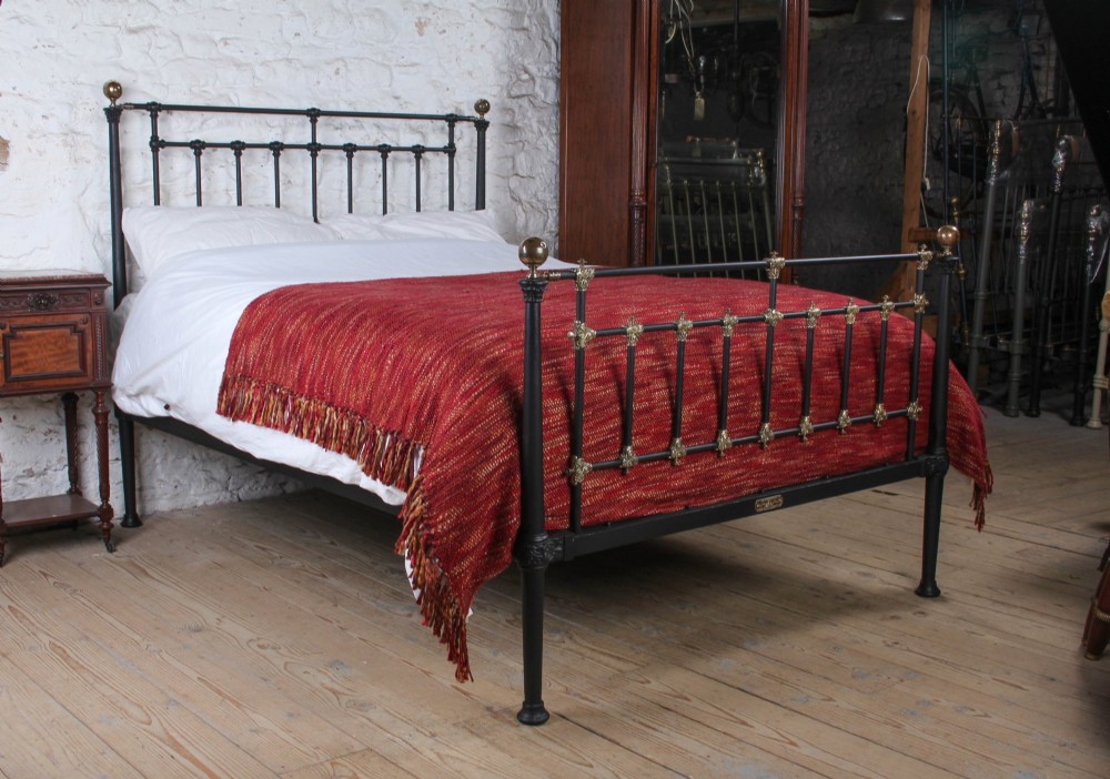 A Victorian black iron and brass king-size bedstead featuring vertical spindles, decorative brass mounts, and brass ball finials.