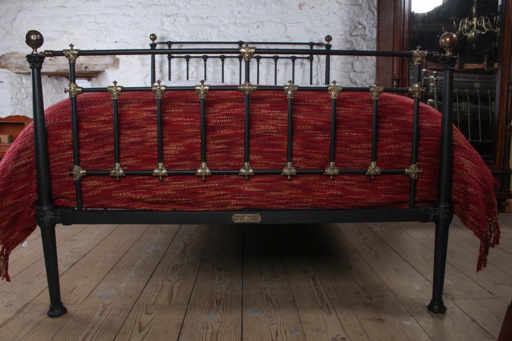 A Victorian black iron and brass king-size bedstead featuring vertical spindles, decorative brass mounts, and brass ball finials. View IV