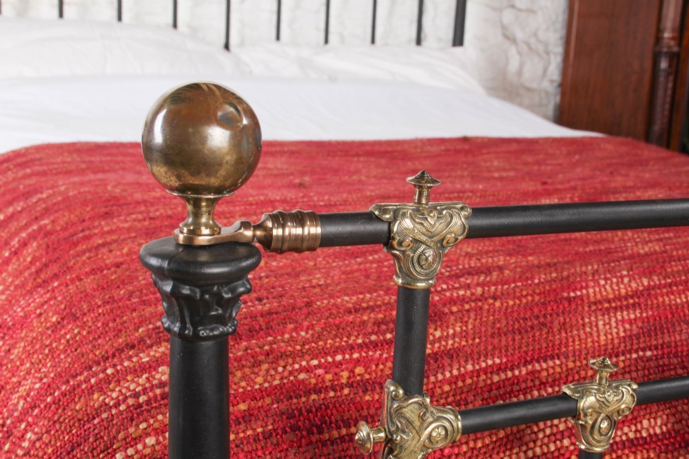A Victorian black iron and brass king-size bedstead featuring vertical spindles, decorative brass mounts, and brass ball finials. View X
